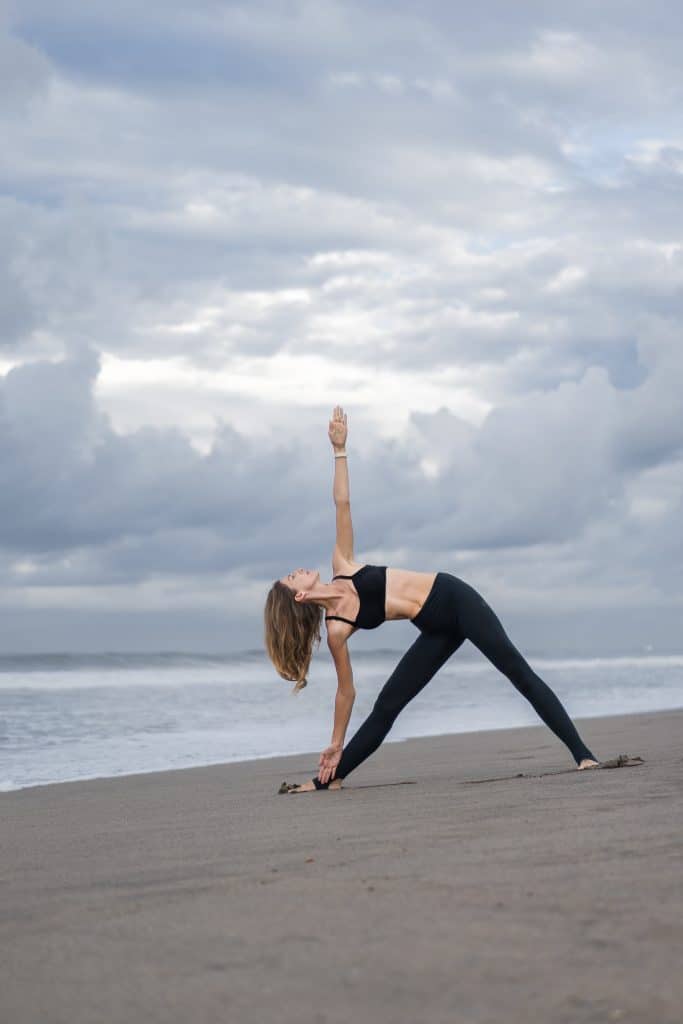 woman doing triangle pose at the beach